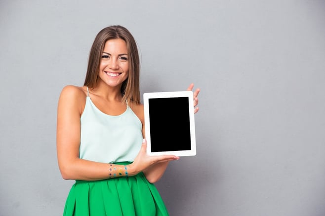 Casual smiling woman showing blank tablet computer screen over gray background. Looking at camera.jpeg